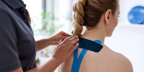 Candid image of an attractive patient during appointment with a professional asian physiotherapist in design kinesiotherapy clinic stretching medical kinesio tape for neck and shoulder pain.